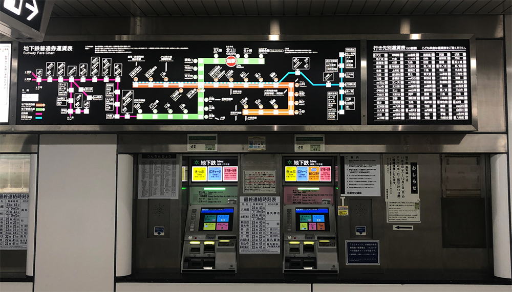 Ticket machines in the Kitayama subway station, with bright lights, maps, and Japanese writing.