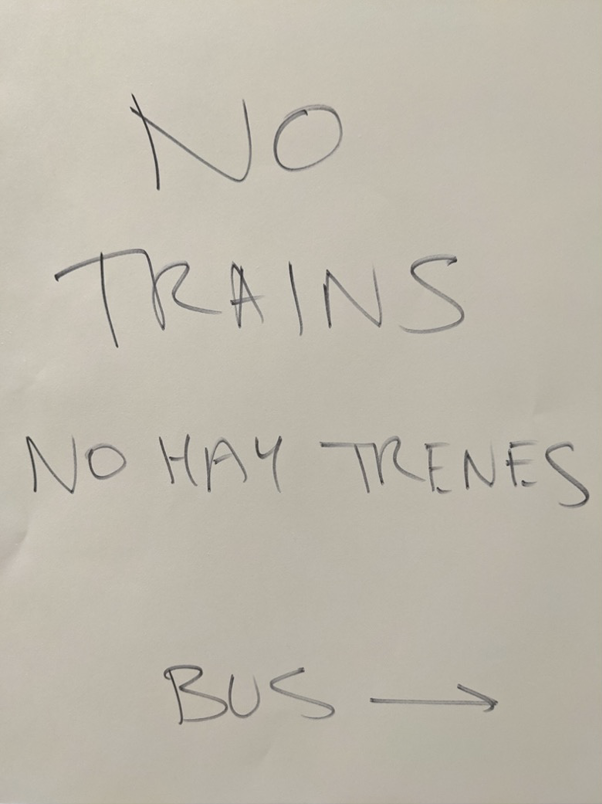 Hastily handwritten sign. The sign says: No Trains, No Hay Trenes, Bus. There is an arrow next to the word "bus."